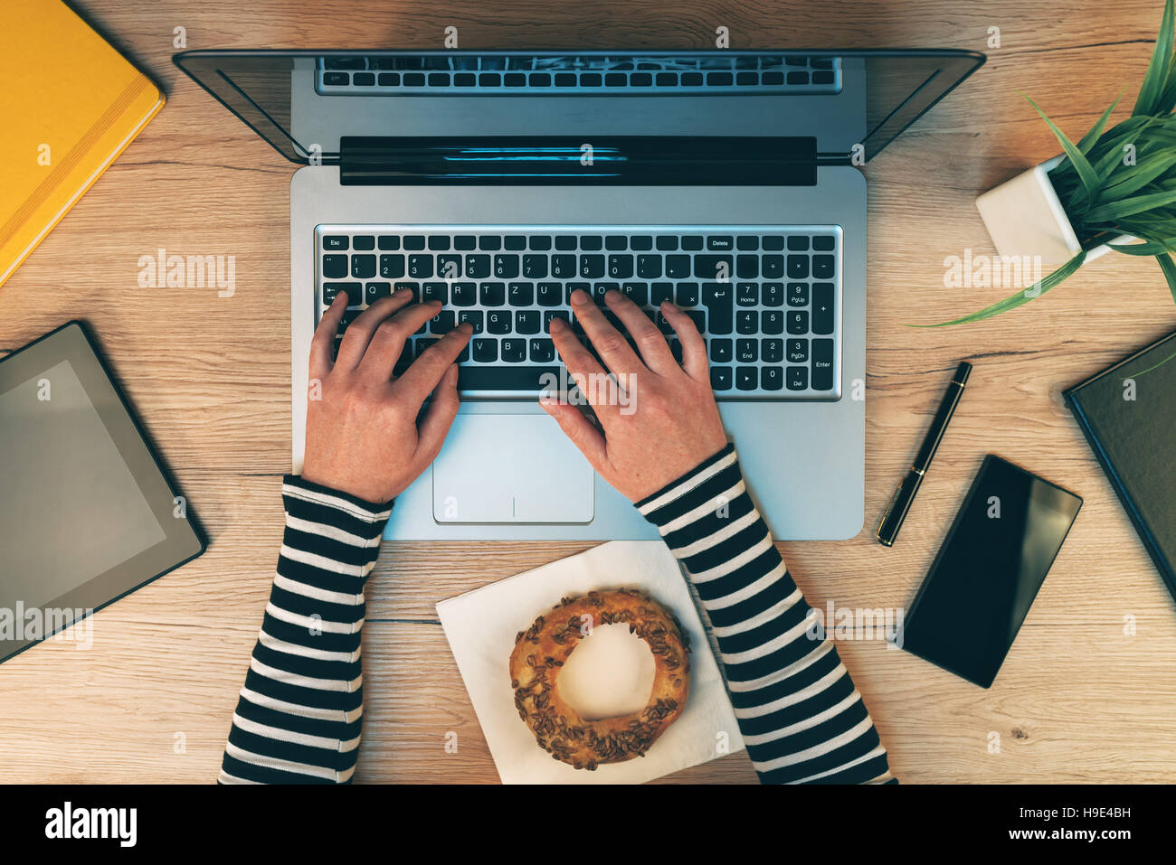 Ufficio quotidiana vita, mani femminili lavorando sul computer portatile - vista superiore di imprenditrice tastiera di digitazione con altra elettronica mobile su area di lavoro d Foto Stock
