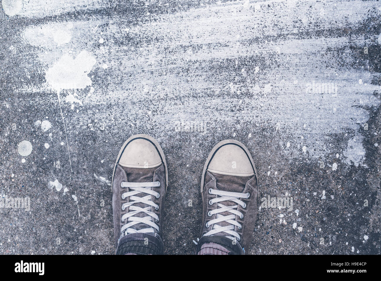 In piedi sul pavimento di cemento con secco bianco pennello macchie, piedini maschio in indossato scarpe sportive su strada Foto Stock