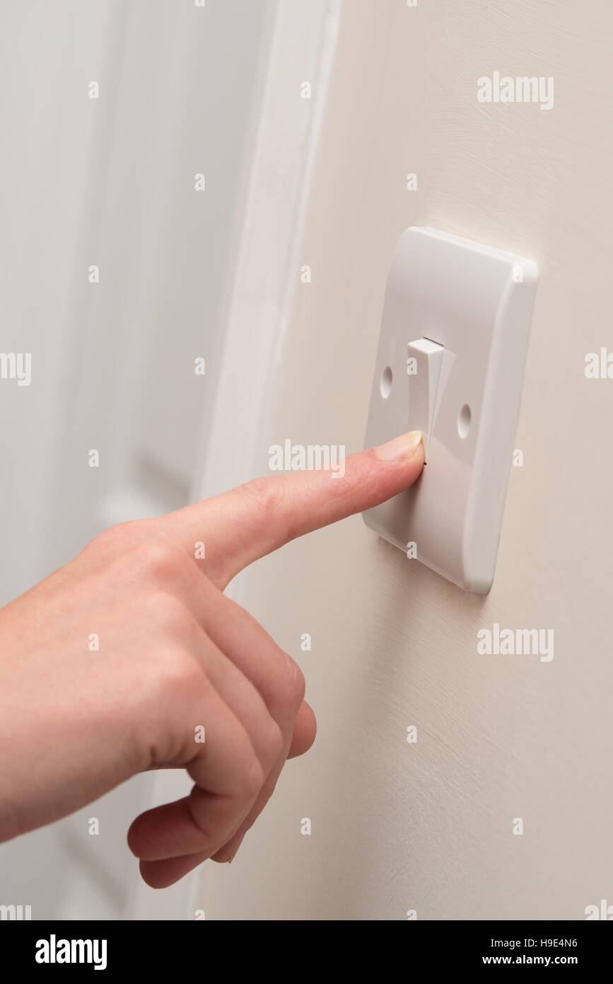 Un dito preme su un unico bianco interruttore luce su una crema parete accanto a un bianco porta in quello che sembra essere un'abitazione domestica Foto Stock