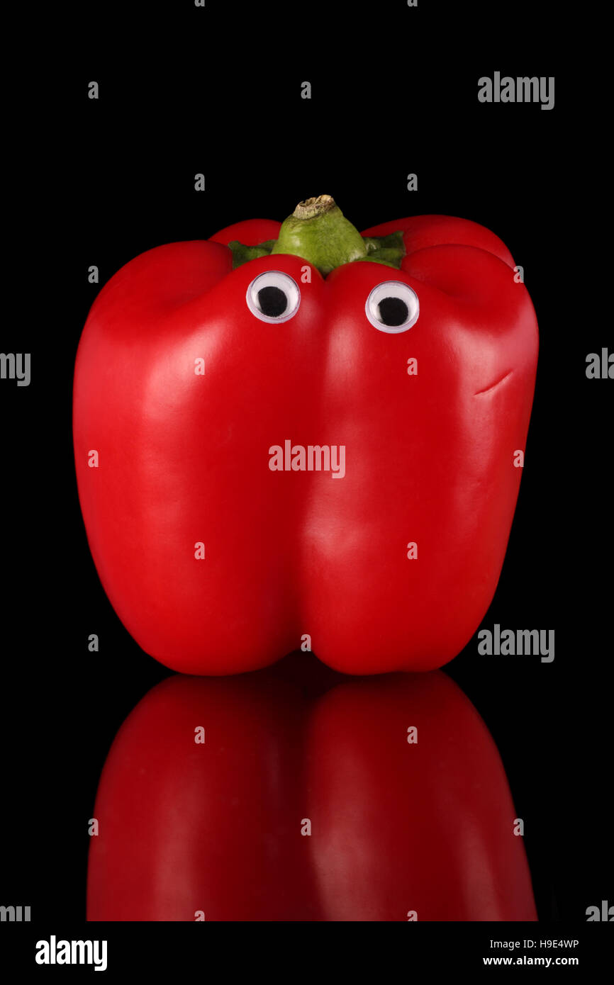 Peperone rosso con occhi comica su uno sfondo nero e la superficie riflettente. Foto Stock