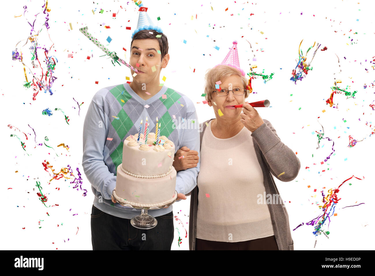 Giovane con una torta di compleanno e una donna matura soffiando parte corna isolati su sfondo bianco Foto Stock