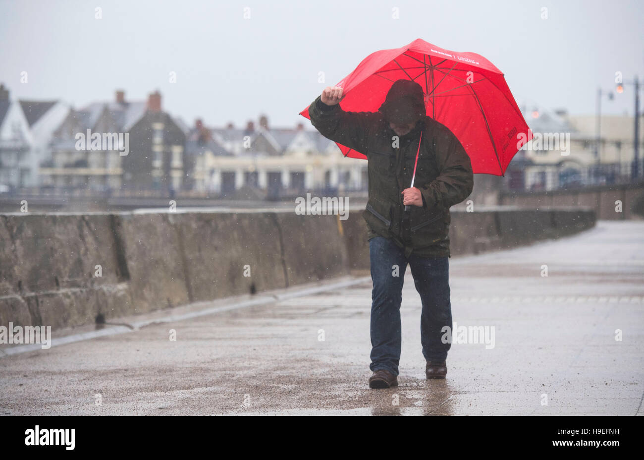 Un uomo di battaglie forti venti con un ombrello rosso durante la tempesta Angus in Porthcawl, South Wales, Regno Unito. Foto Stock