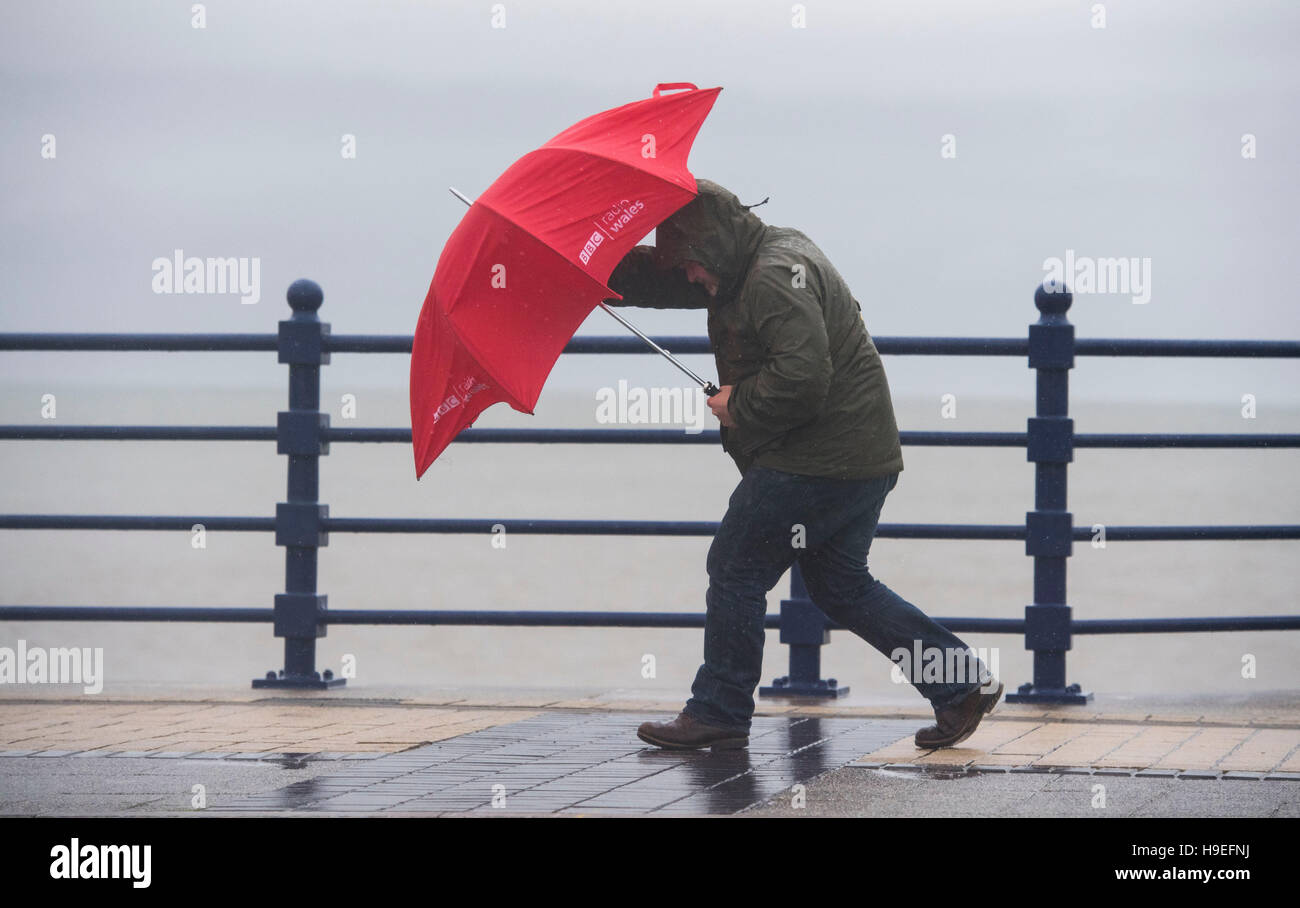 Un uomo di battaglie forti venti con un ombrello rosso durante la tempesta Angus in Porthcawl, South Wales, Regno Unito. Foto Stock