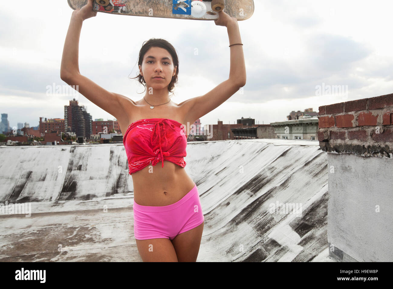 Razza mista giovane donna sul tetto azienda skateboard Foto Stock