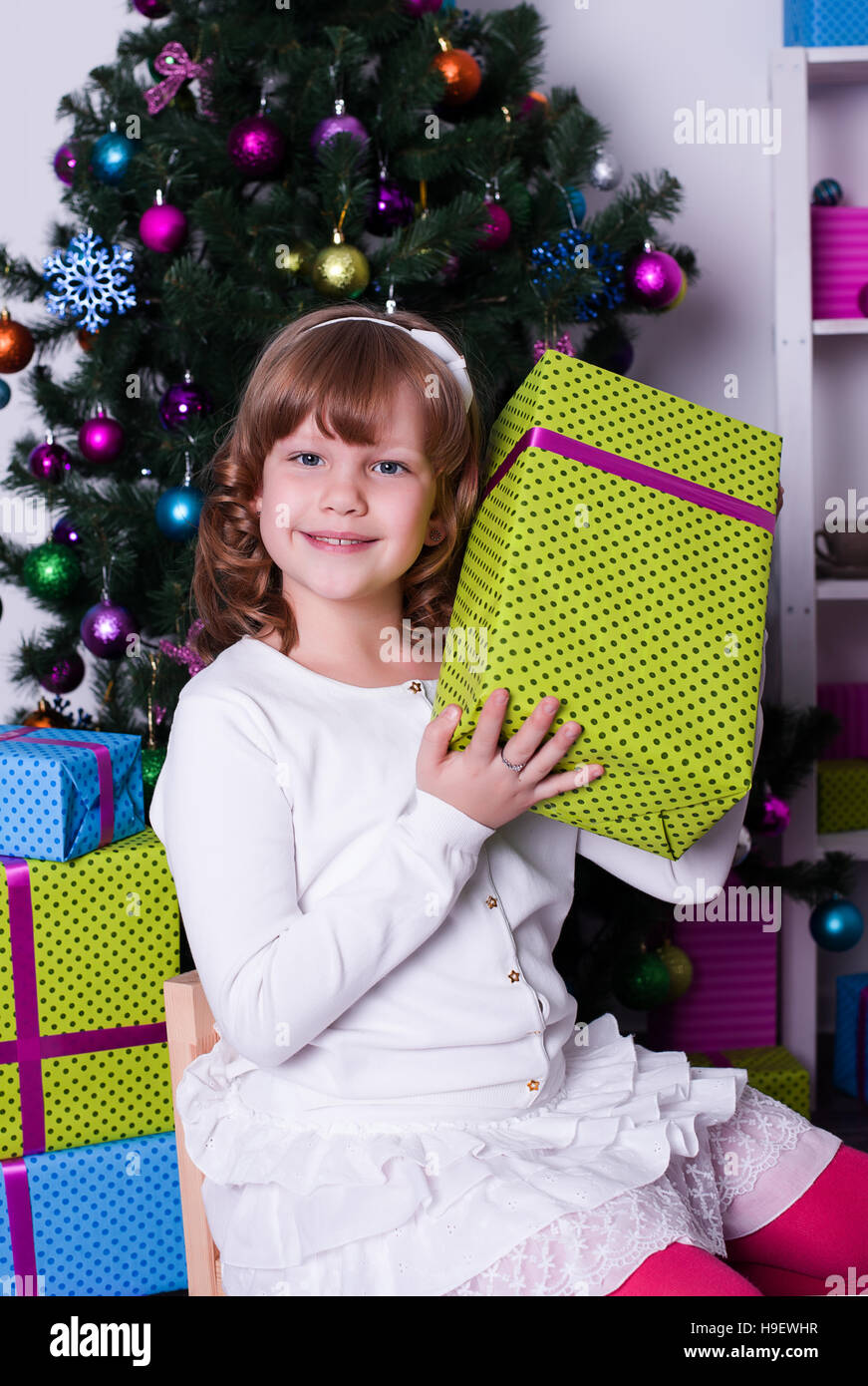 Una ragazza con un dono seduta vicino ad albero di Natale Foto Stock