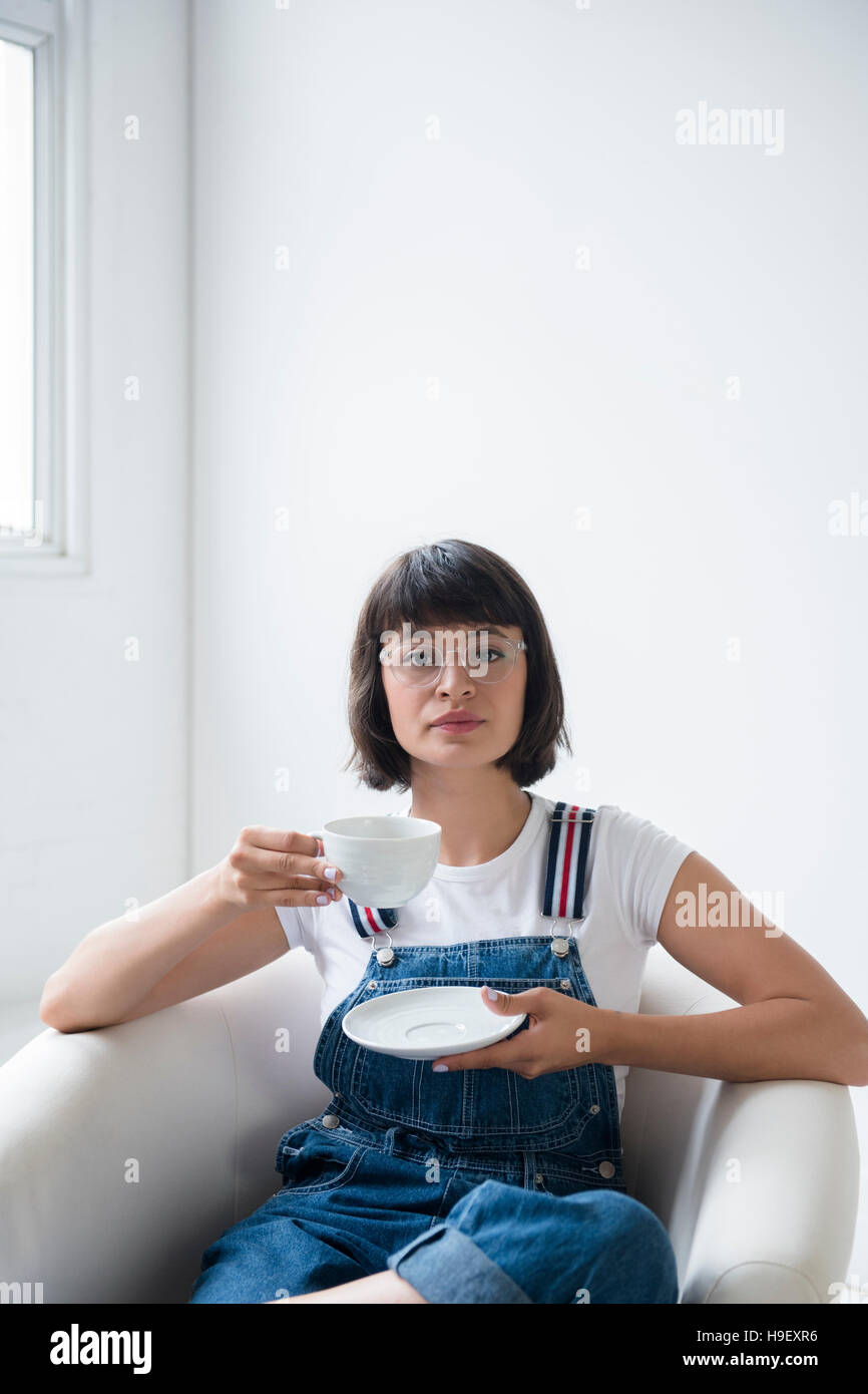 Ritratto di donna ispanica di bere il caffè in poltrona Foto Stock