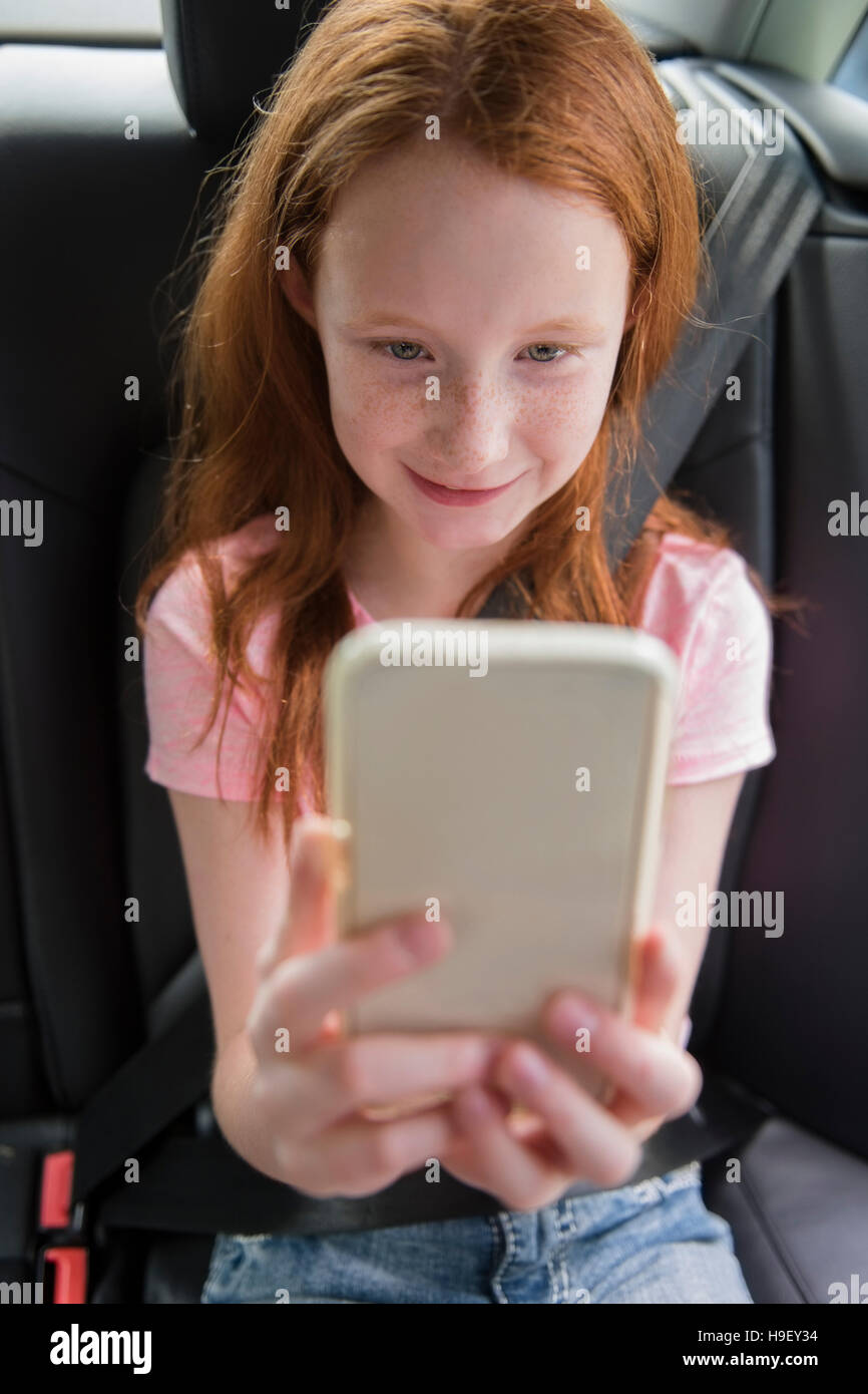 Sorridente ragazza caucasica texting sul telefono cellulare in auto Foto Stock