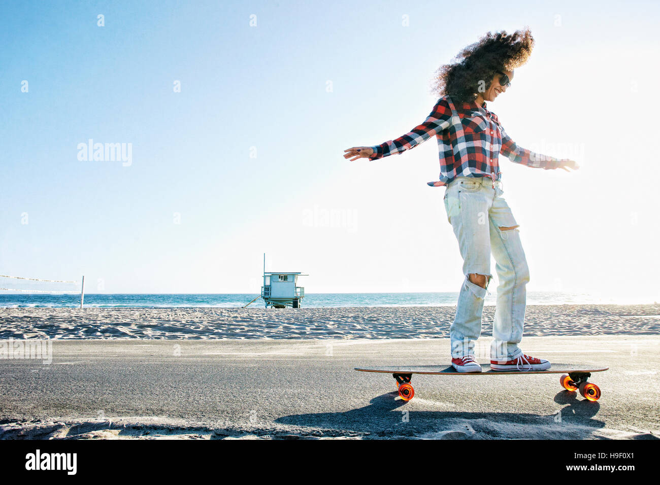 Donna ispanica skateboard equitazione presso la spiaggia Foto Stock