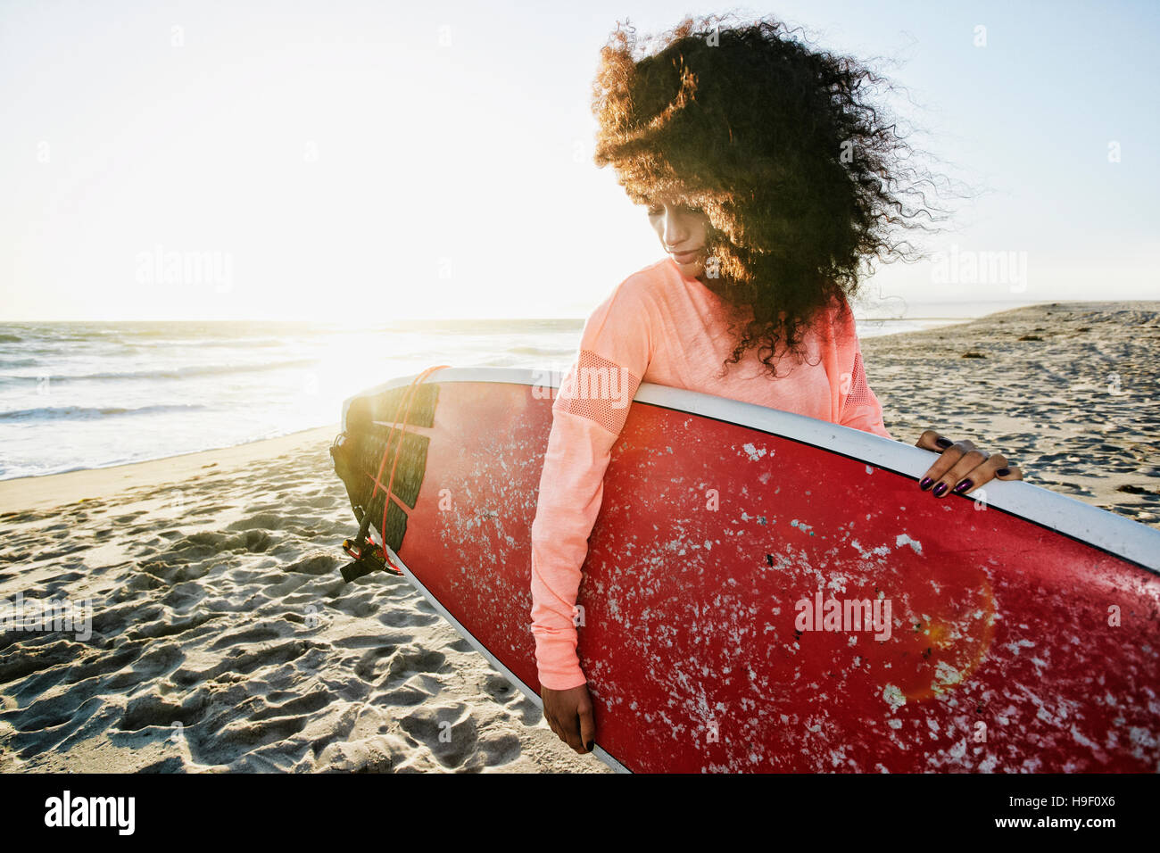 Donna ispanica tenendo la tavola da surf in spiaggia Foto Stock