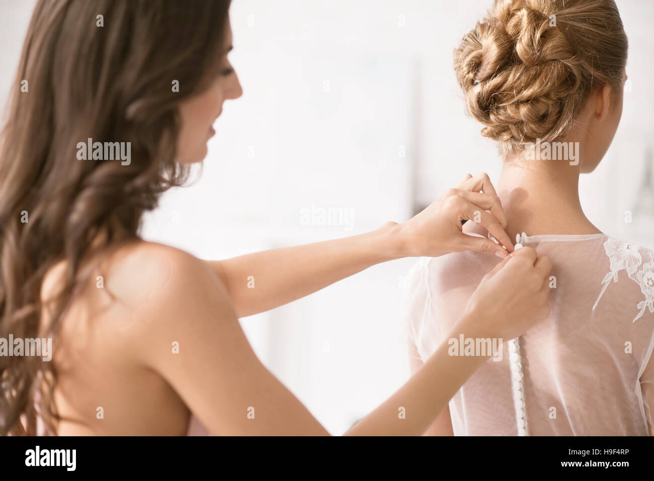 Incantevole damigella aiutando la sposa con il suo abito Foto Stock