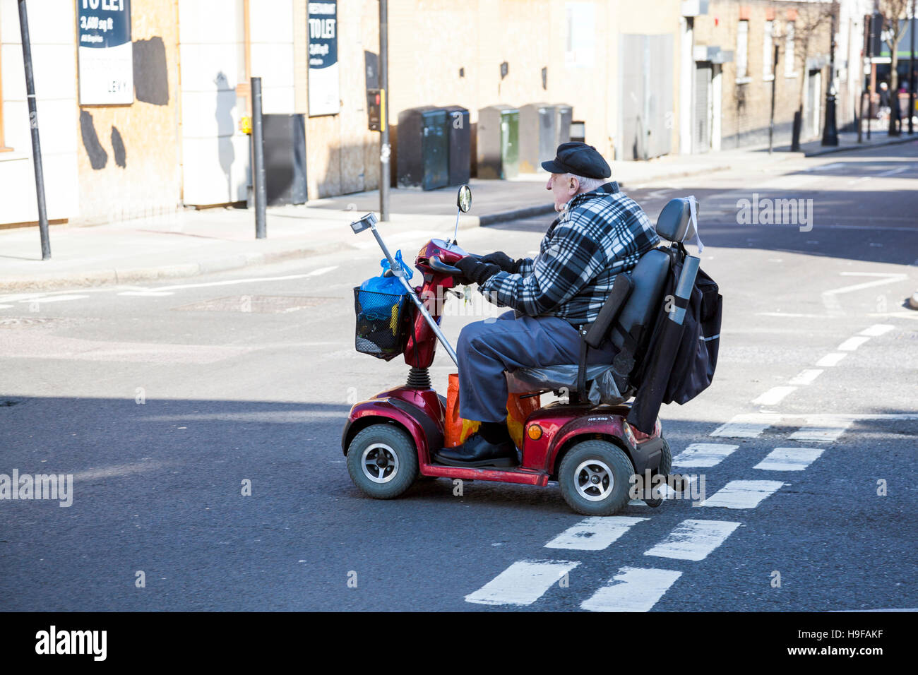 Un anziano uomo alla guida di uno scooter di mobilità su strada Foto Stock