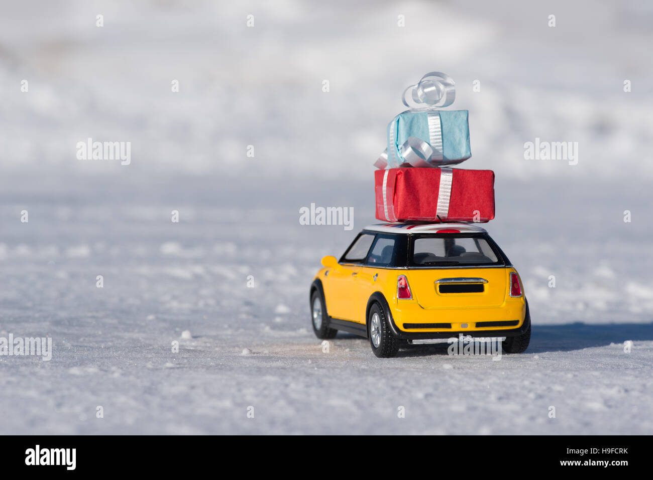Piccolo giallo giocattolo auto portante avvolto regali di natale nella neve Foto Stock