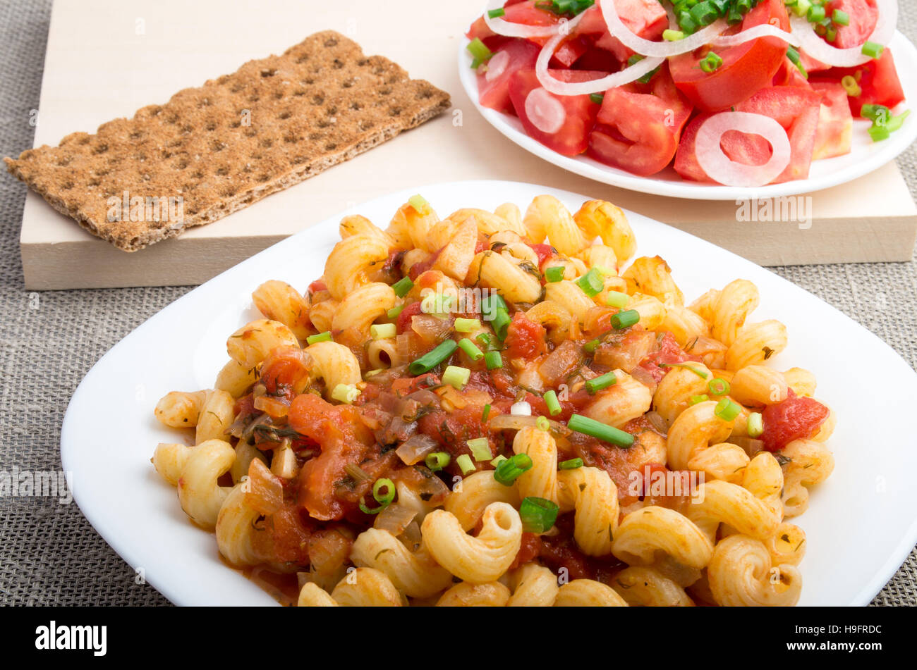 La pasta cotta cavatappi con legumi stufati e salsa di porri servito con insalata di pomodori e pane di segale su sfondo tessili Foto Stock