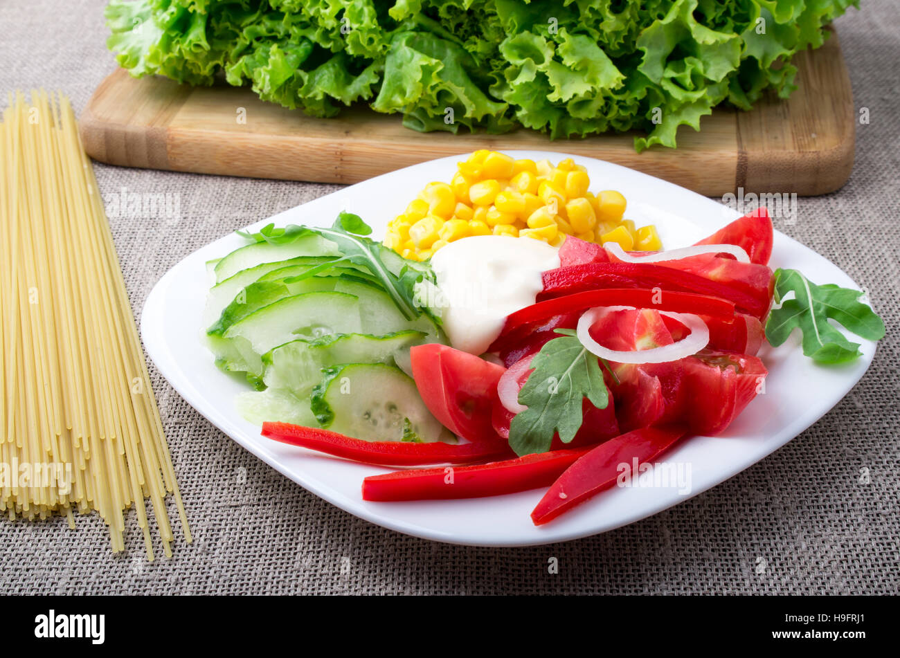 Vegetariano fresca insalata di verdure crude senza trattamento termico su una piastra bianca accanto alla lattuga e spaghetti su uno sfondo di colore grigio tablec Foto Stock