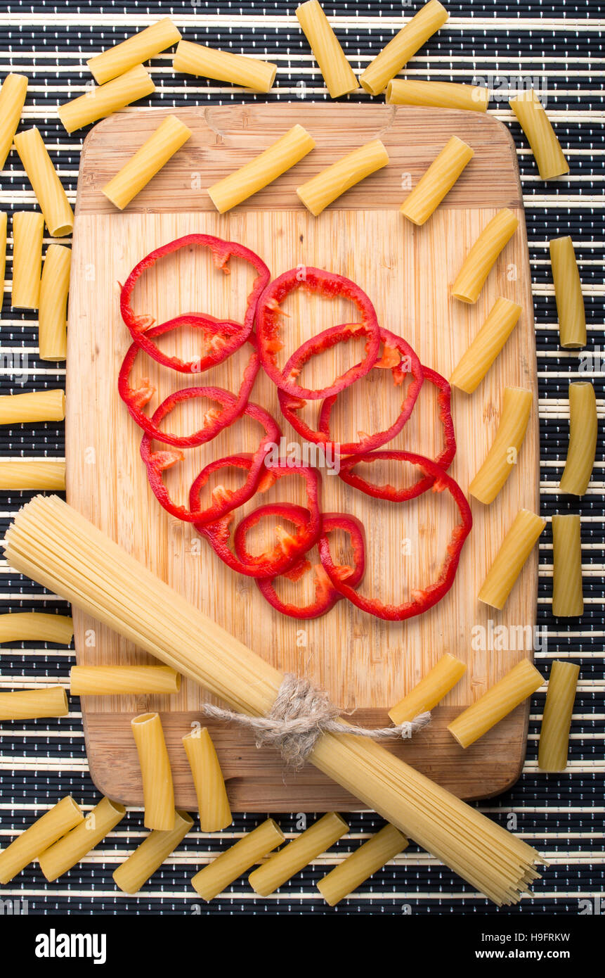 Vista verticale su sfondo di cibo da pasta e campana rosso-peperone per una sana cottura su una base di legno su uno sfondo a strisce Foto Stock