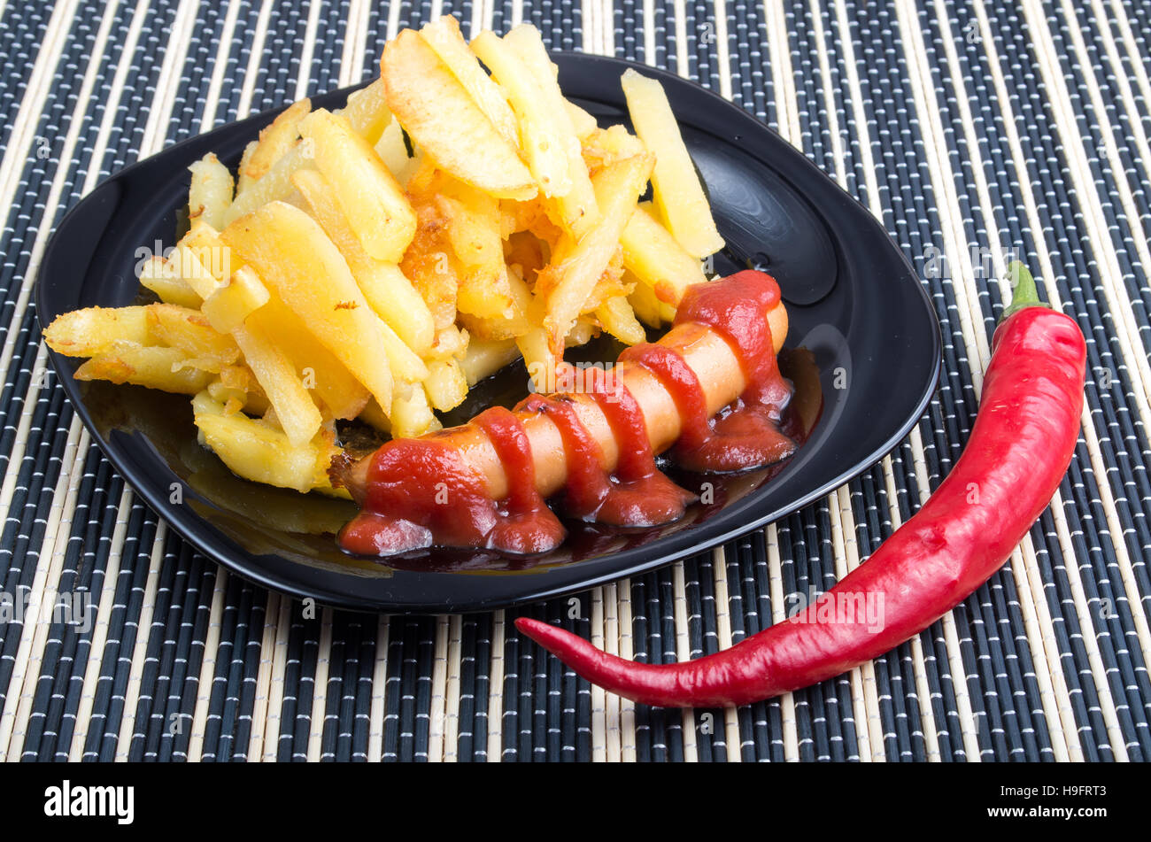 Il pranzo piatti fatti con ingredienti naturali - una porzione di patatine fritte e salsiccia con il ketchup accanto a pod caldo rosso pepe Foto Stock
