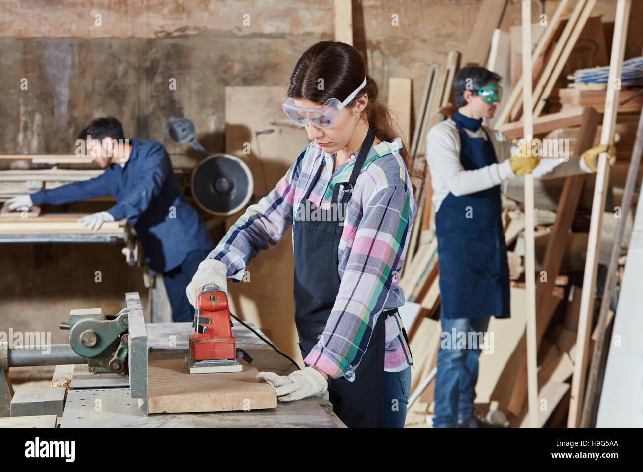 La donna come falegname con smerigliatrice a mano al negozio di falegnameria Foto Stock