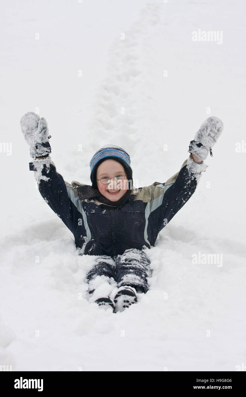 Sette-anno-vecchio ragazzo seduto nella neve Foto Stock