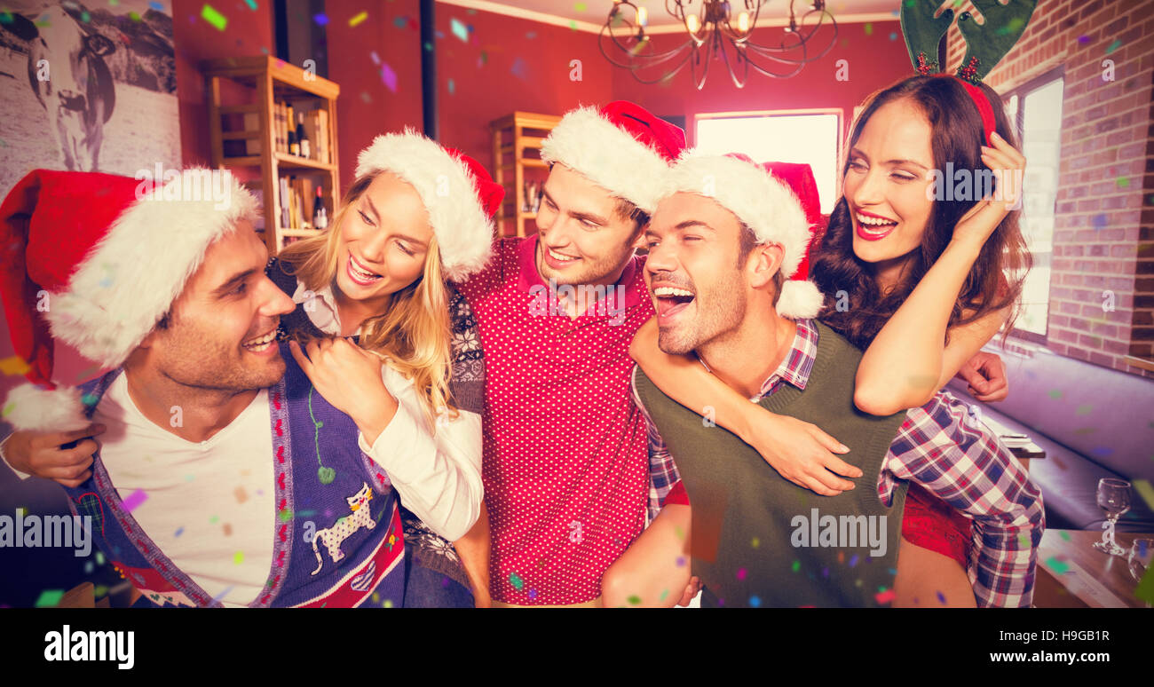Immagine composita di uomini che indossano il natale indossando dando alle donne piggyback rides Foto Stock