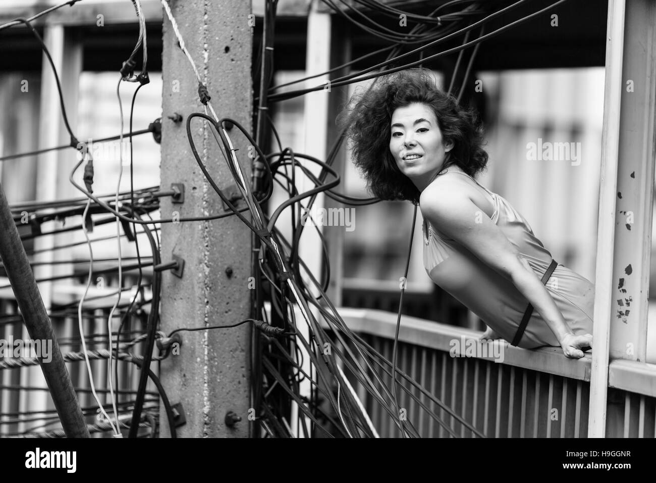 Giovane donna asiatica in piedi sul cavalcavia in background dei fasci di fili, ritratto in bianco e nero. Asia, urbanizzazione, industriale, metrop Foto Stock