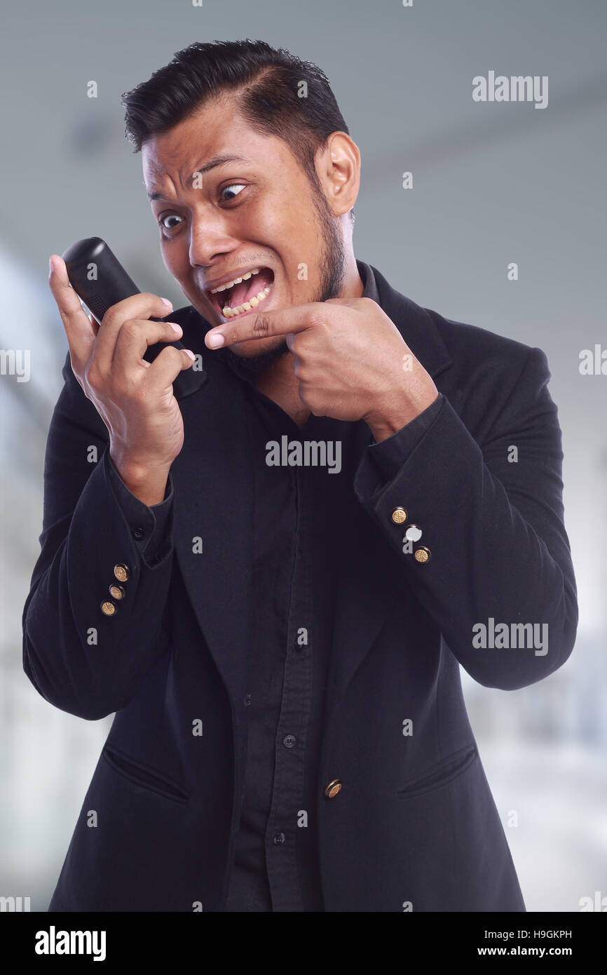 Gli uomini che mostra la sua espressione gridando faccia mentre egli puntando il dito sul telefono isolato su sfondo bianco Foto Stock