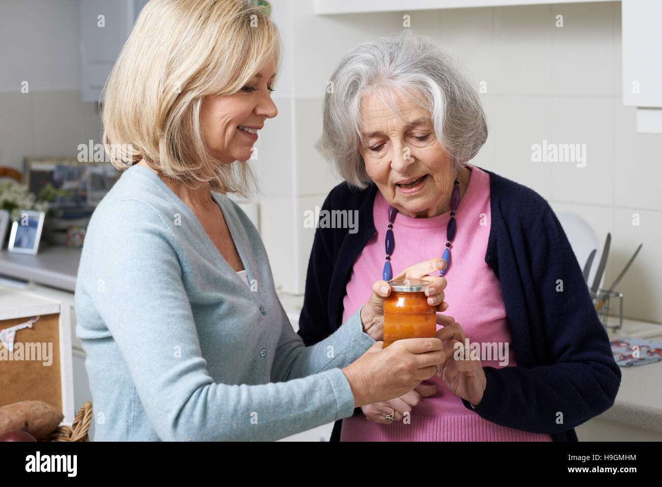 Donna aiutando Senior prossimo per rimuovere il coperchio di vaso Foto Stock
