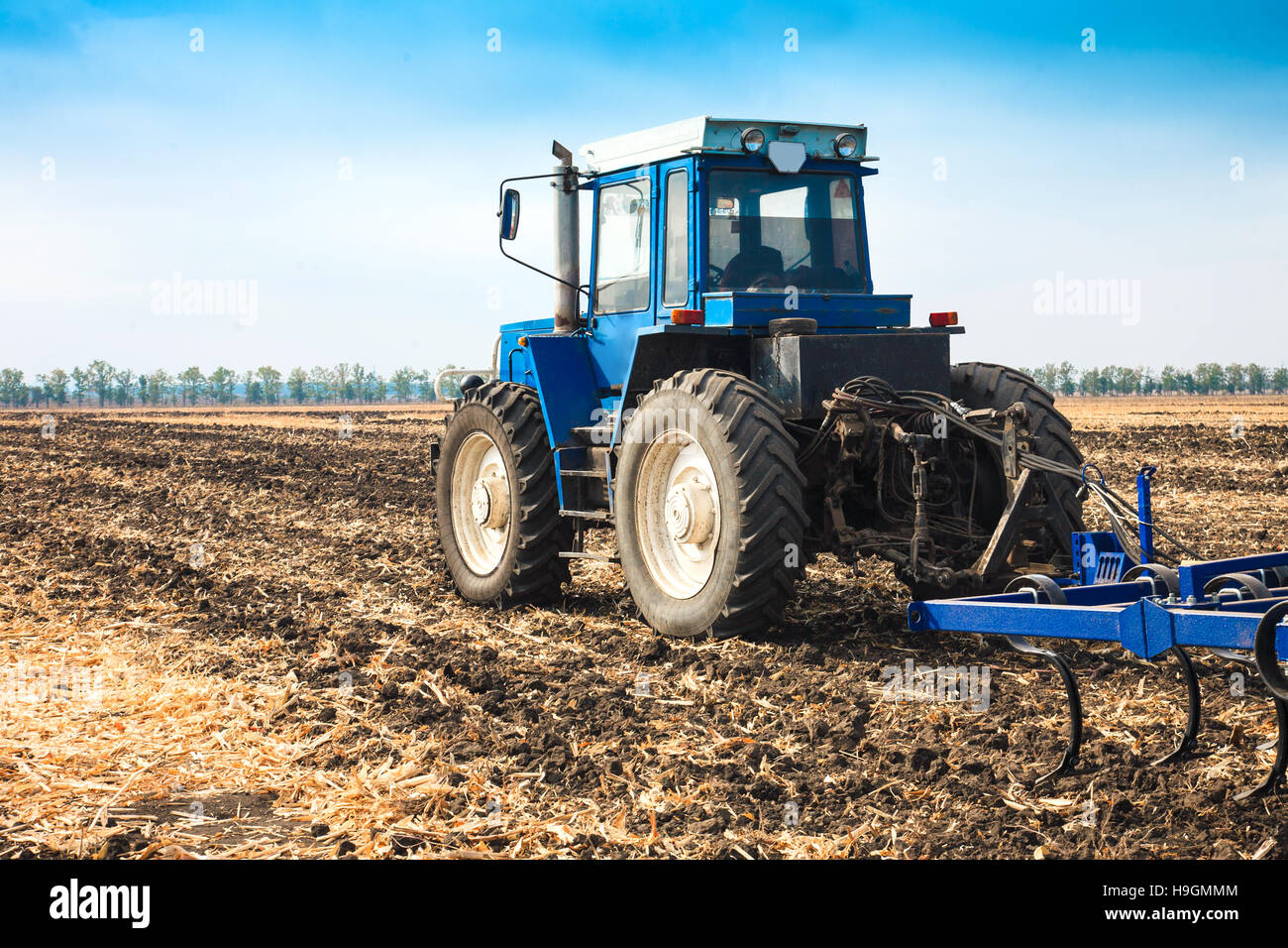 Vecchio Blu trattore con un aratro in un campo in una giornata di sole. Il concetto di lavoro in campi di agricoltura e industria. Foto Stock