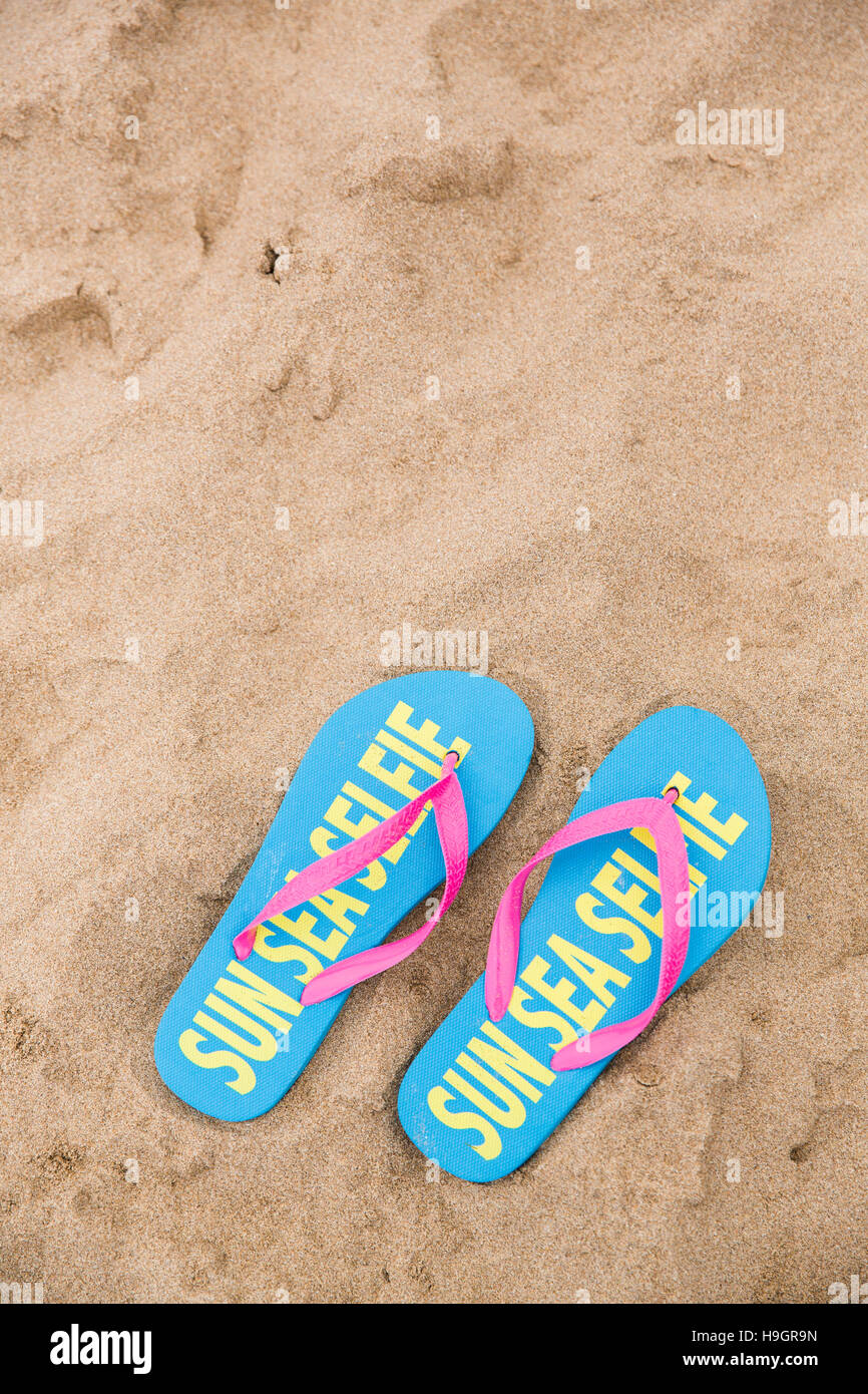 Coppia di flip flop con 'Sun mare Selfie' scritto su di loro su di una spiaggia di sabbia. Foto Stock