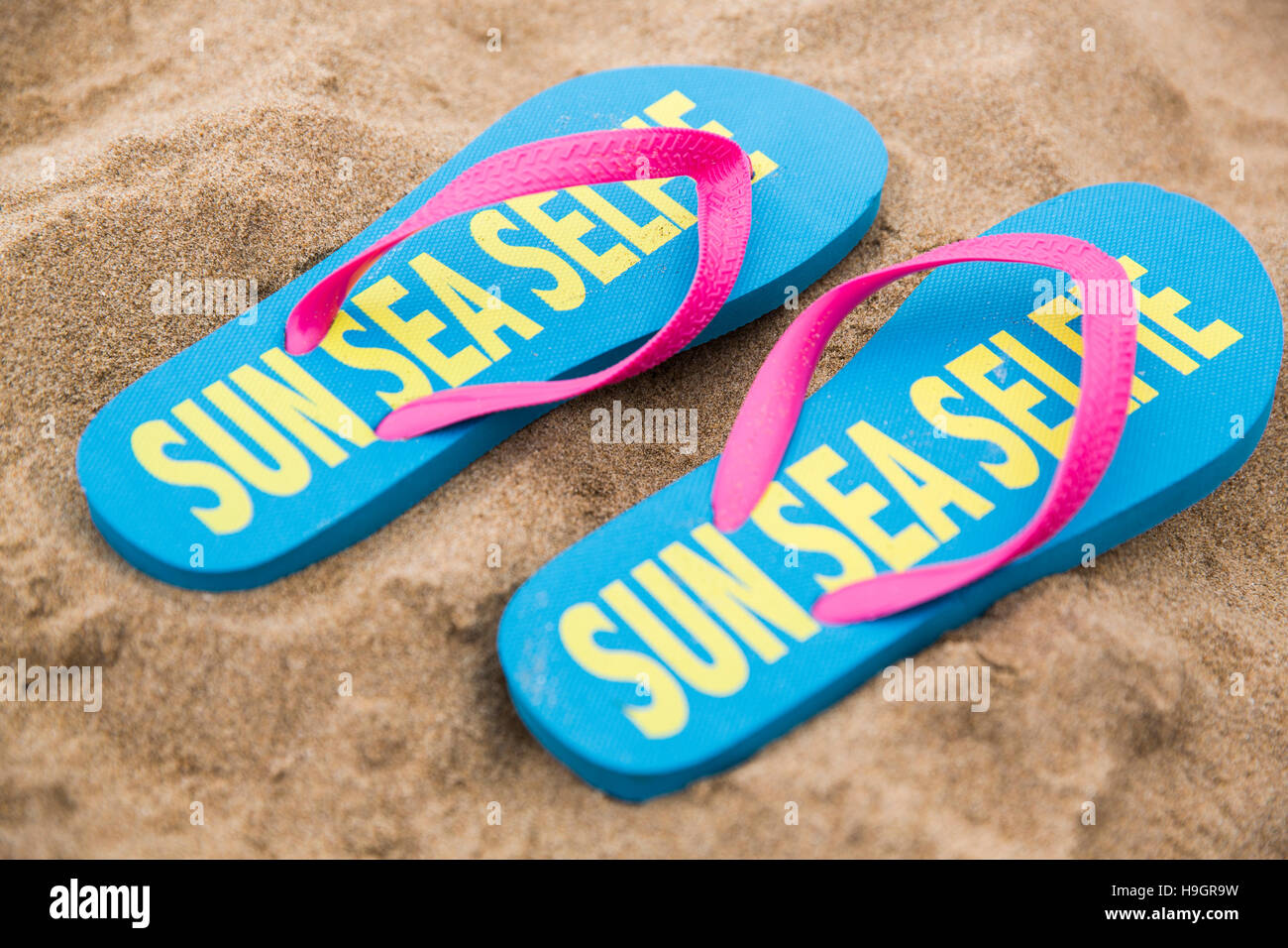 Coppia di flip flop con 'Sun mare Selfie' scritto su di loro su di una spiaggia di sabbia. Foto Stock