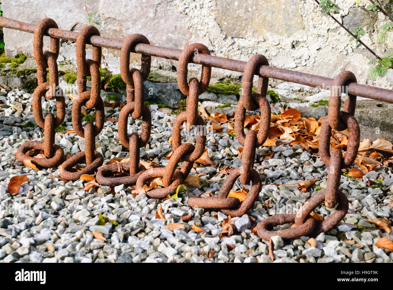 Rusty catene su una barra di ferro utilizzato per livellare un percorso di pietra. Foto Stock