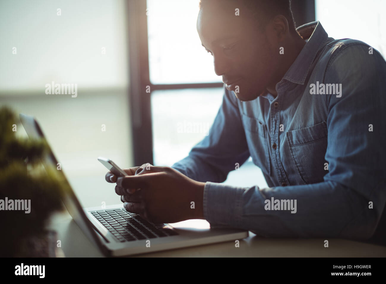 Dirigente aziendale utilizzando il telefono cellulare mentre si lavora sul computer portatile Foto Stock