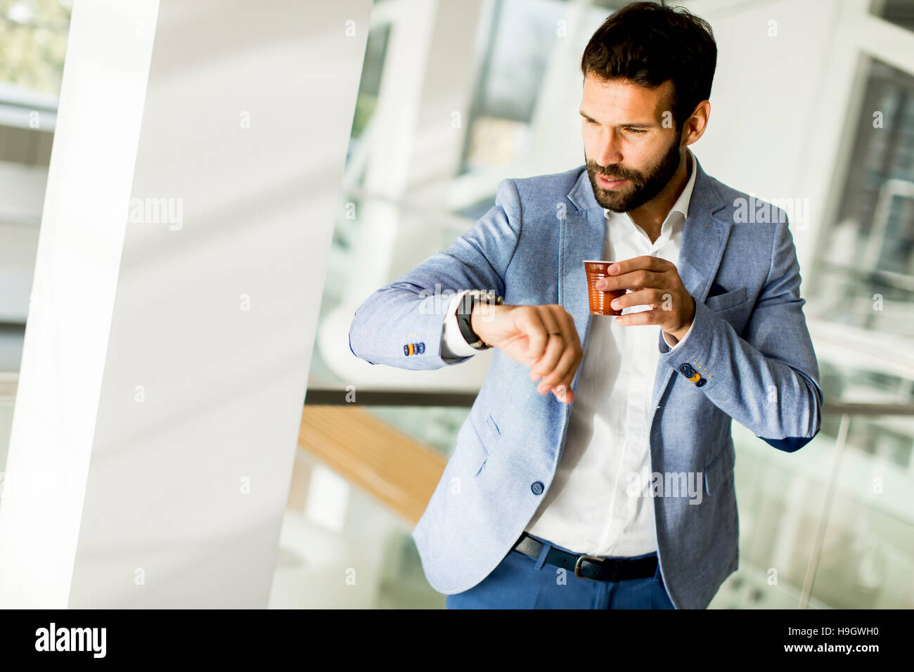 Business man in un business suit , una tazza di caffè in un edificio per uffici e guardando l'orologio Foto Stock