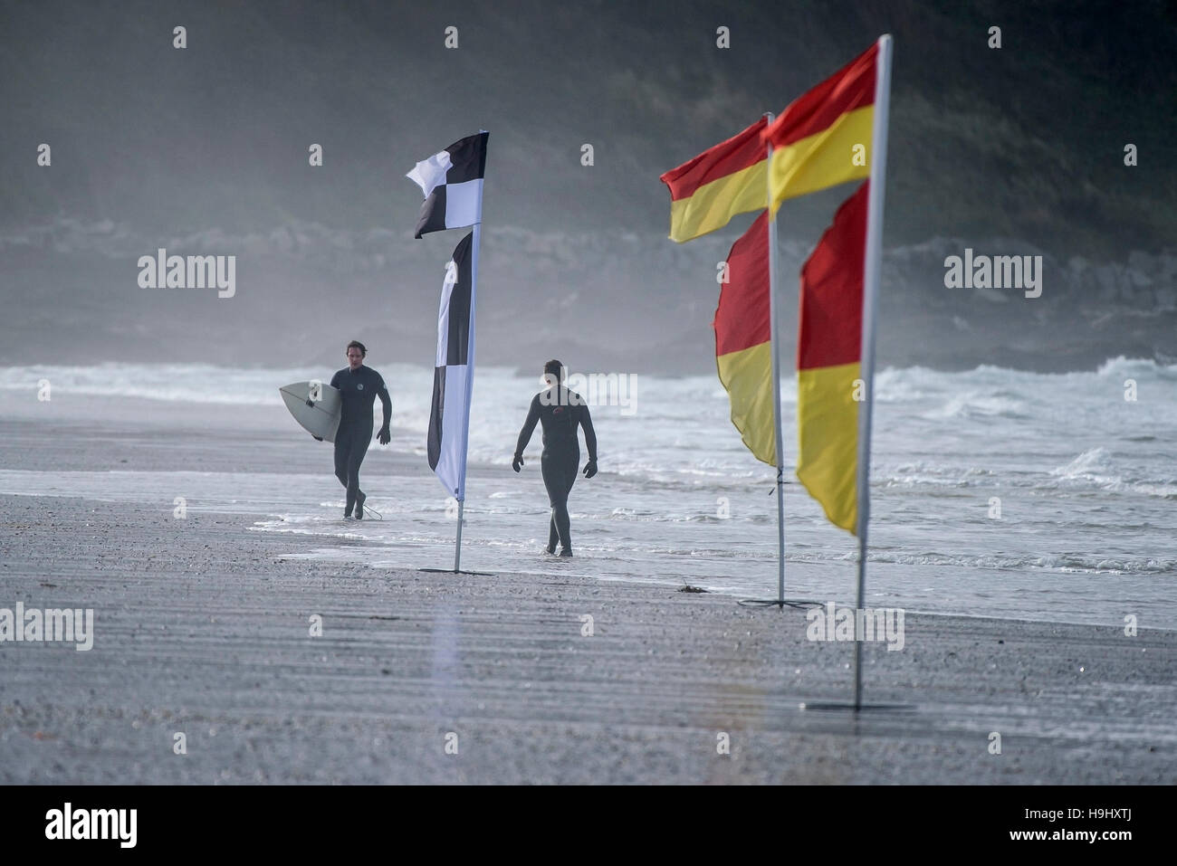 Surfers camminare vicino a bandiere di sicurezza su Fistral Beach in Newquay, Cornwall. Foto Stock