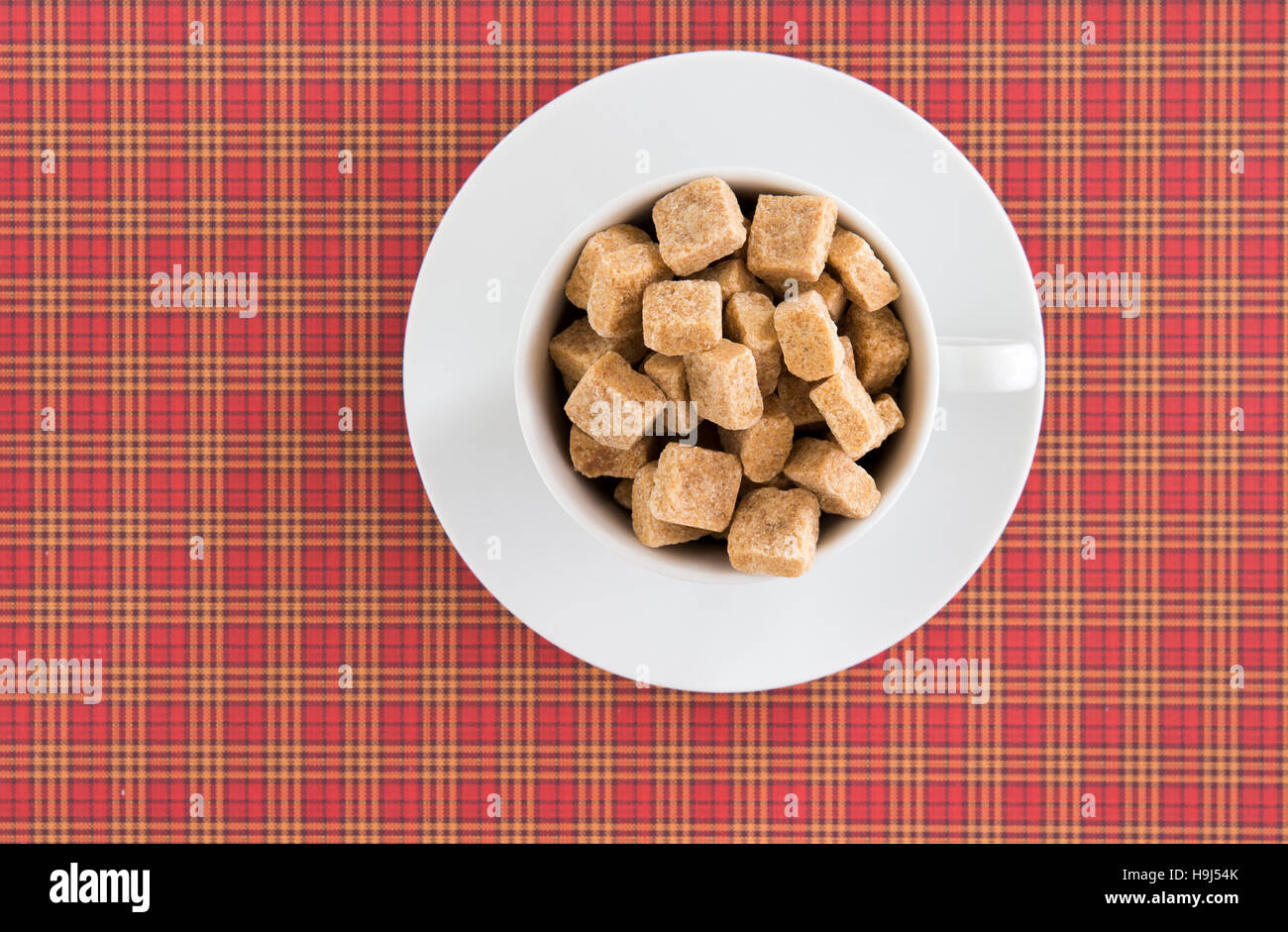 Vista superiore del bianco di caffè o di tè coppa piena di zucchero di canna i cubi su rosso sfondo squadrato. Dieta dolce unhealty concetto di dipendenza Foto Stock