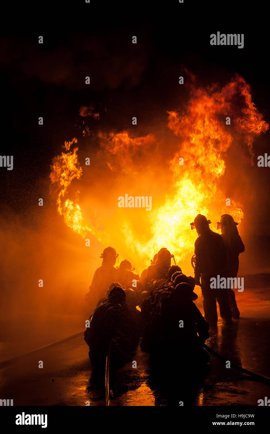 Silhouette di vigili del fuoco nella lotta contro un furioso incendio con enormi fiamme di bruciare il legname Foto Stock