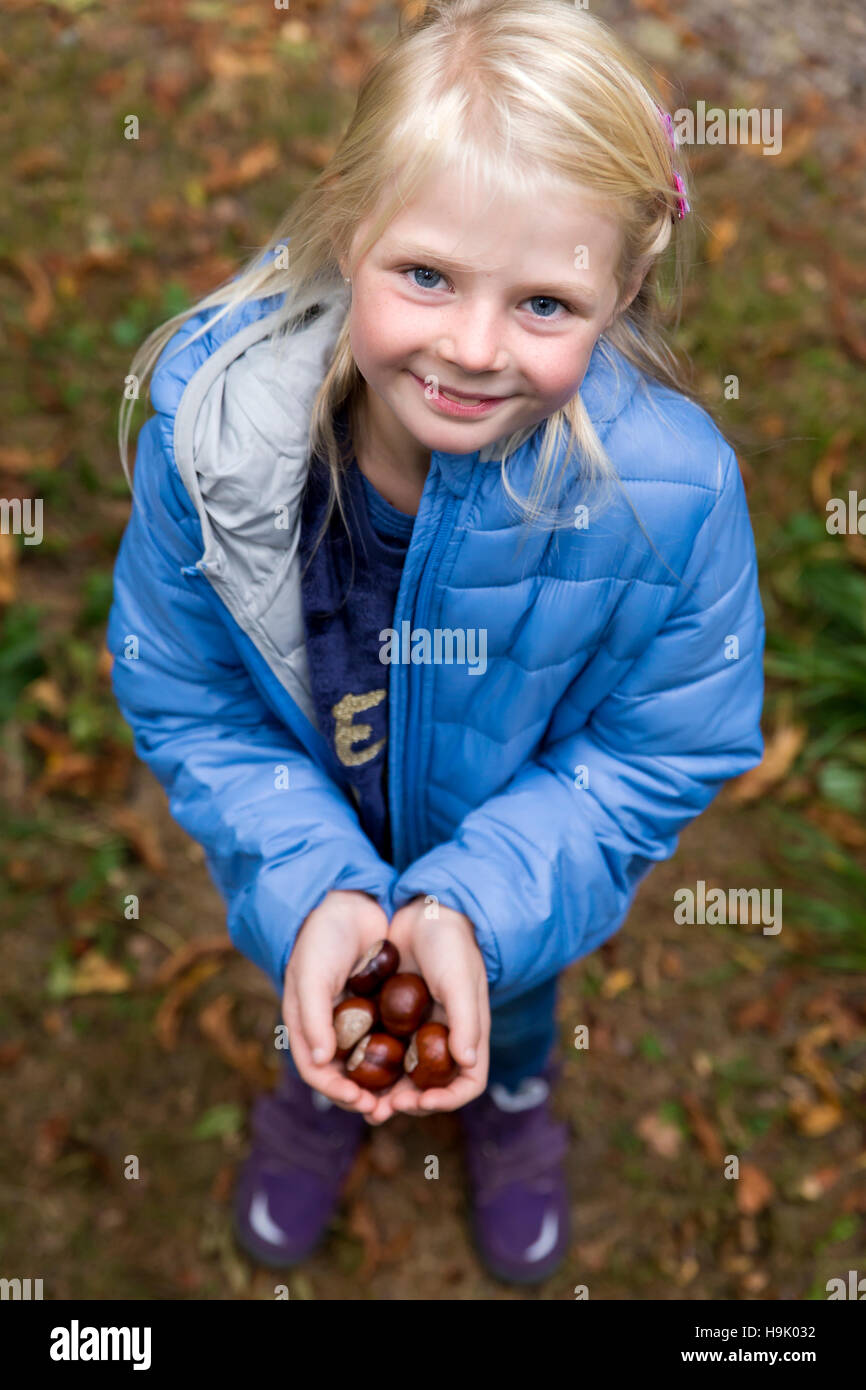 Ritratto di bionda sorridente bambina tenendo le castagne nelle sue mani Foto Stock
