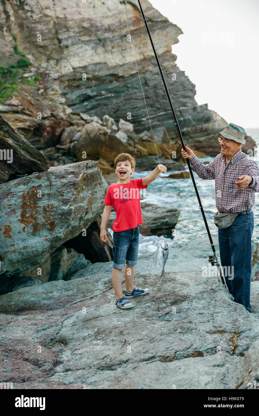 Felice ragazzo tenendo il pesce sulla linea di pesca catturati da suo nonno Foto Stock