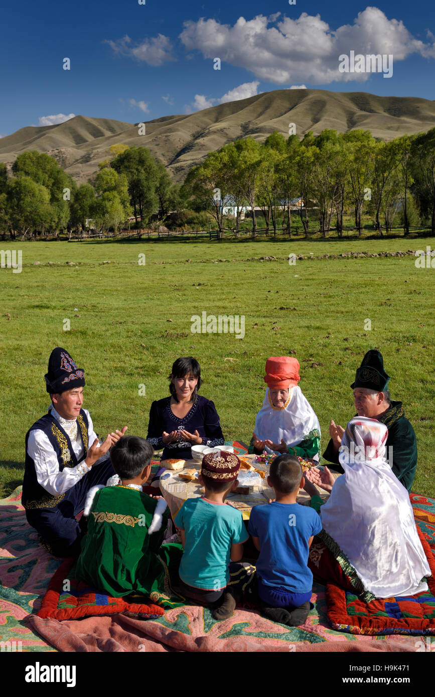 Famiglia kazako in abiti tradizionali pregare prima di mangiare a un picnic in soggiornare Kazakistan Foto Stock