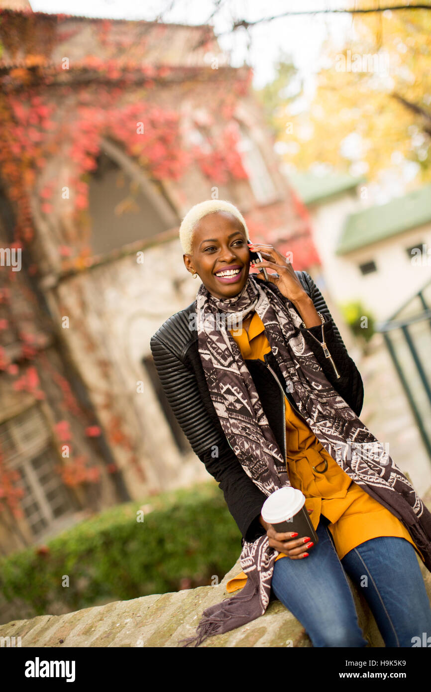 Moderno e giovane africano donna americana in posa con caffè di andare e il telefono cellulare all'aperto Foto Stock