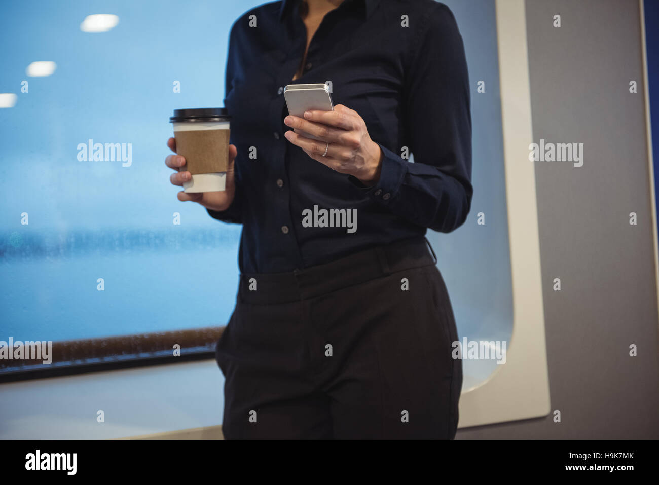 Imprenditrice con tazza di caffè usando il telefono mentre sta in piedi in treno Foto Stock