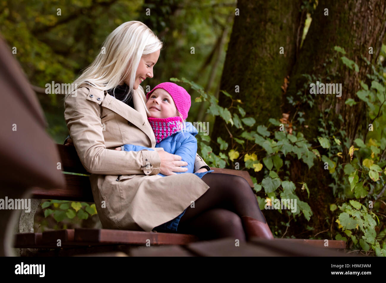 Madre e figlia piccola seduta su una panchina in foresta autunnale Foto Stock