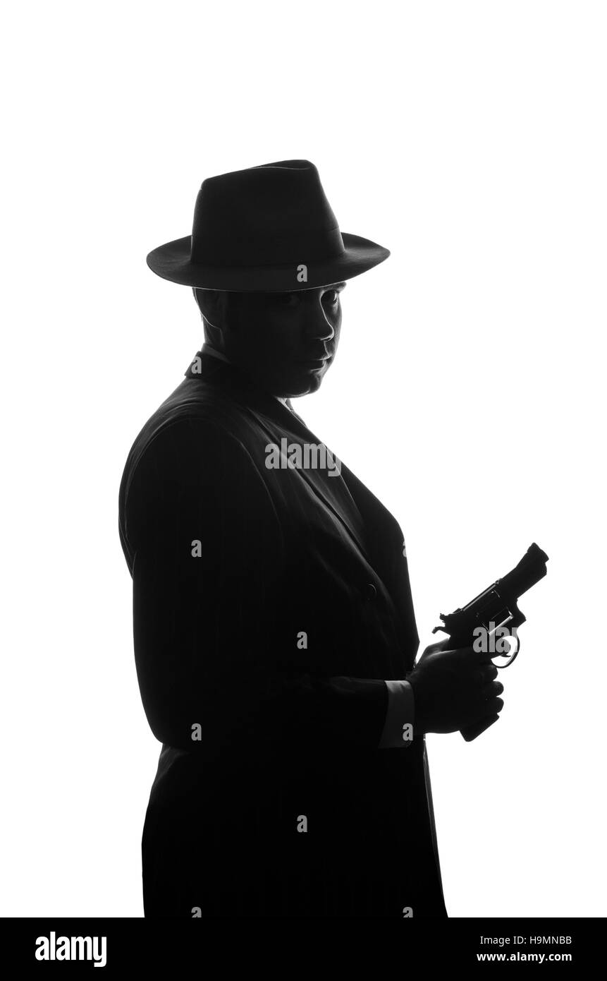 Silhouette di detective privato con una pistola in mano destra. Soggiorno agente di lato alla fotocamera e guarda come mafioso Al Capone. Scena criminale. Studio shot Foto Stock