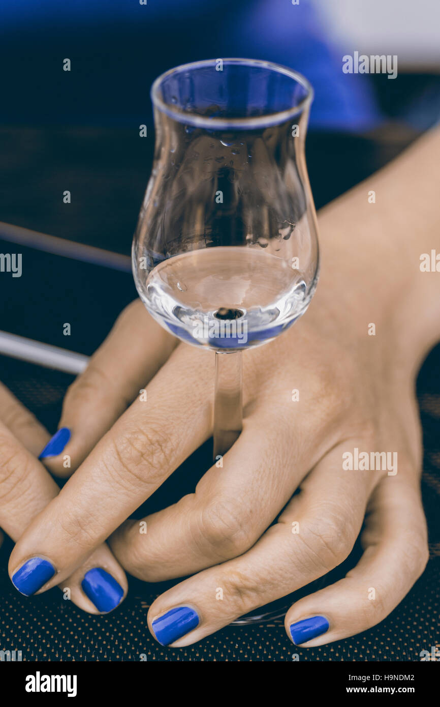 Un bicchierino di grappa in donna con le mani in mano. Acquavite di uve o di grappa sul tavolo. Foto Stock