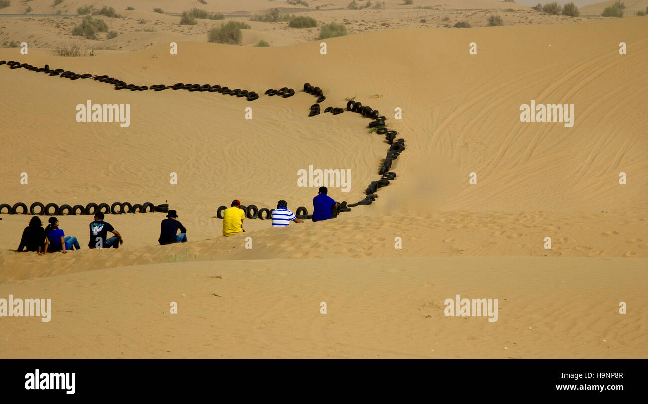 Un gruppo di giovani amici seduti insieme in un deserto a Dubai, Emirati arabi uniti Foto Stock