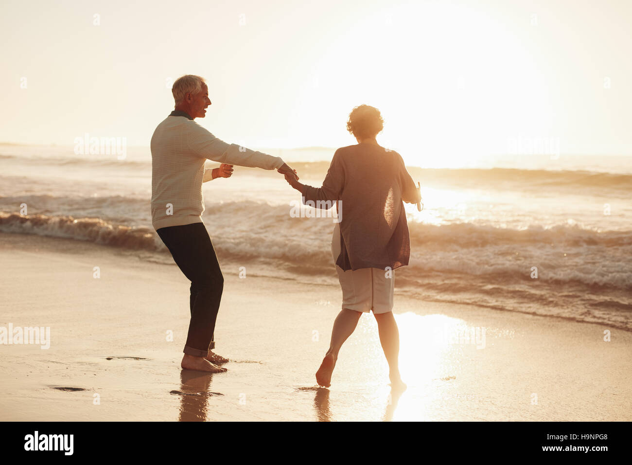A piena lunghezza shot di coppia senior per divertirsi in spiaggia durante il tramonto. Coppia matura godendo le vacanze insieme al mare. Foto Stock
