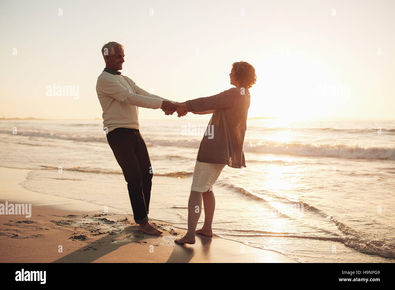 Amorevole coppia senior per mano e godere di una romantica giornata in riva al mare. Senior l uomo e la donna giovane tenendo le mani al tramonto sulla spiaggia. Foto Stock