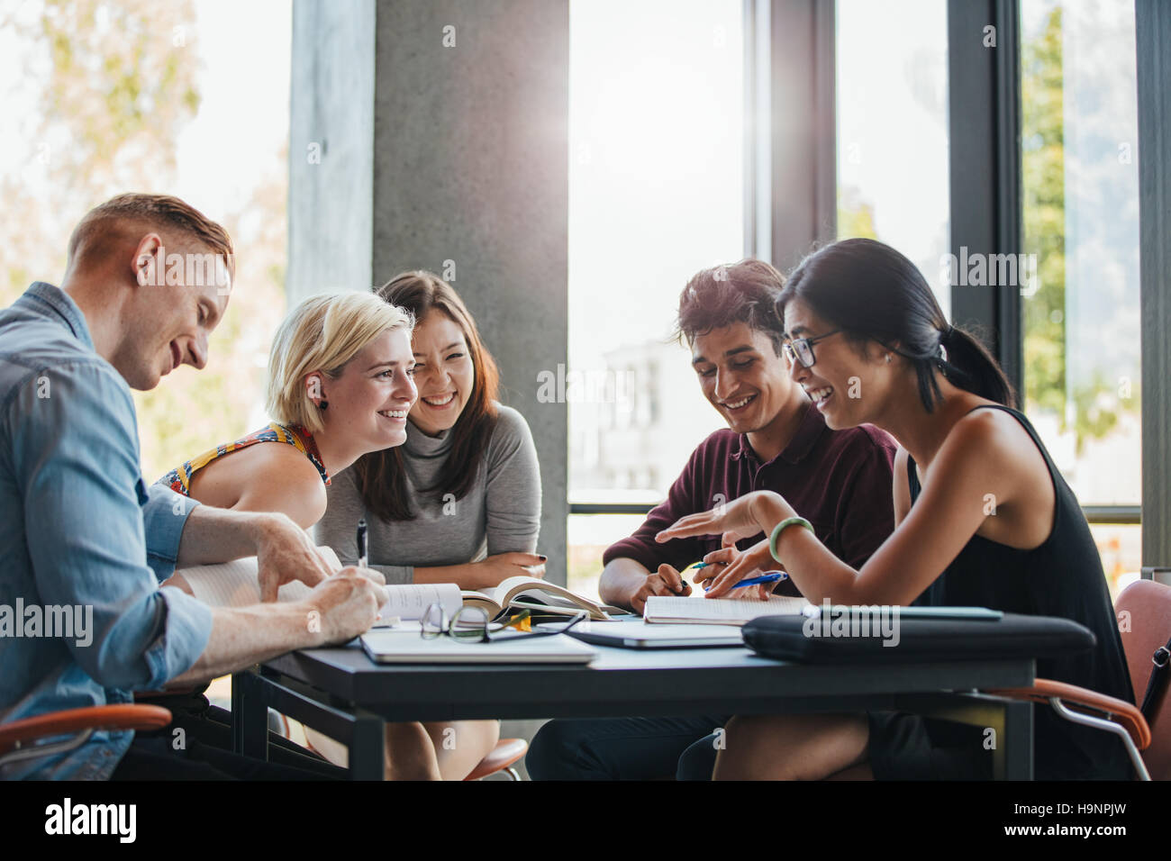 Contenti i giovani studenti universitari che studiano con libri in biblioteca. Un gruppo di persone e multirazziale in college library. Foto Stock