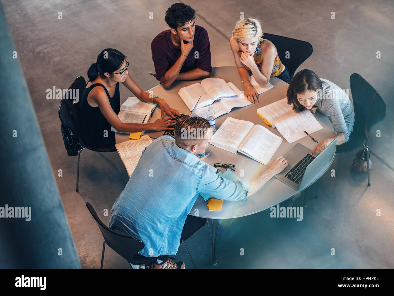 Ripresa ad angolo alto di giovani uomini e donne seduti a tavola con libri che usano un computer portatile. studenti universitari che studiano di gruppo. Foto Stock