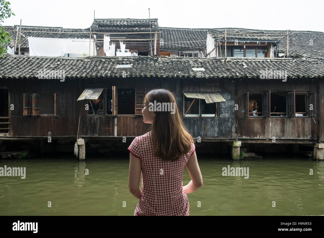 Cina, Wuzhen, Xizha Scenic Area, ragazza seduta sul bordo del fiume Foto Stock