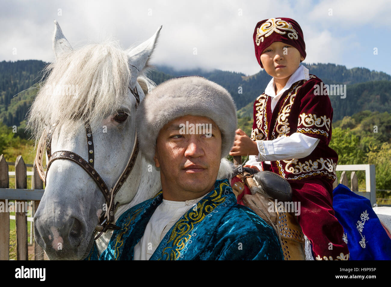 Padre e figlio kazako sul cavallo in abiti tradizionali alla mostra kazako di giochi nazionali ad Almaty, Kazakhstan Foto Stock